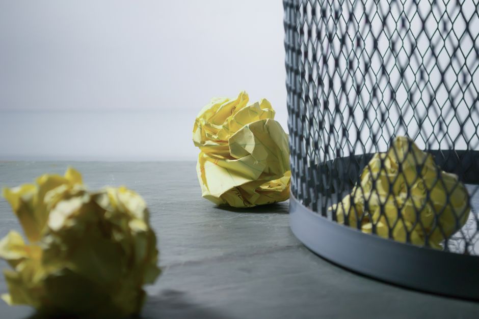 A close-up view of a white woven polypropylene sack filled with a variety of discarded plastic bottles and containers, some crumpled and others intact, with labels and caps still attached. The bottles